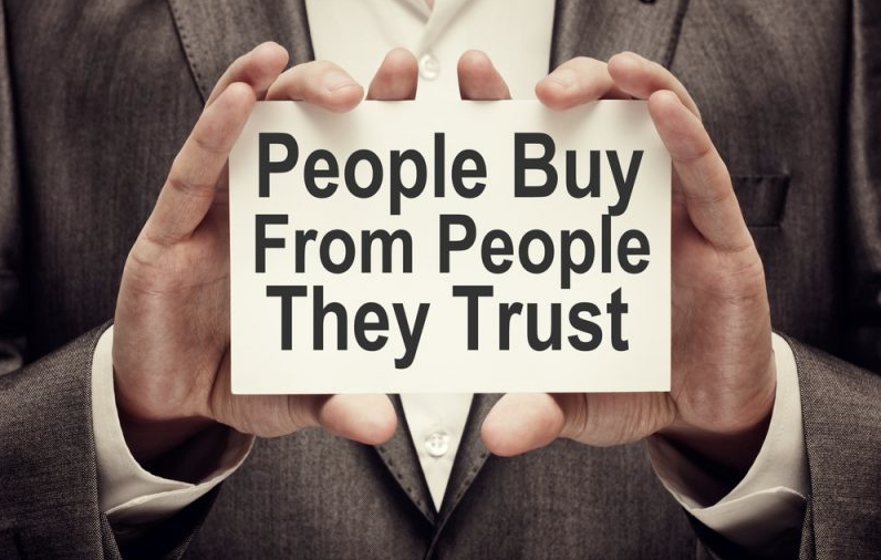 Close up of the hands of a man in suit holding a card that says "people buy from people they trust"